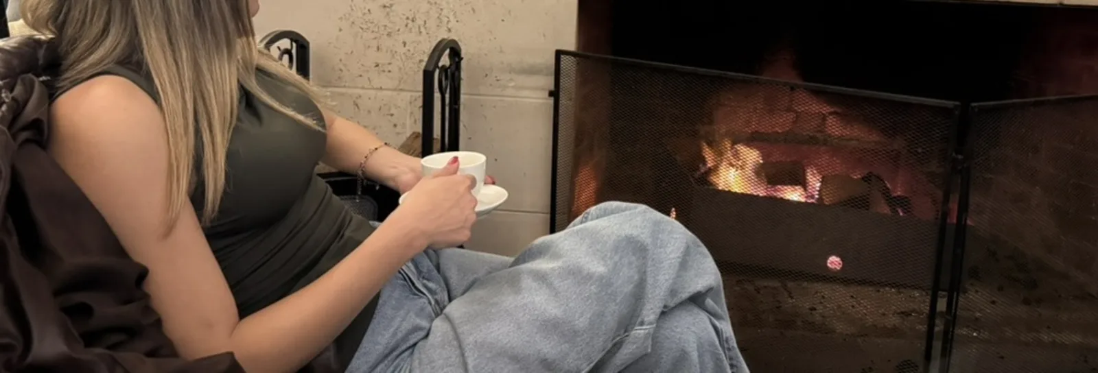 A cup of tea held in both hands, beside a lit fireplace